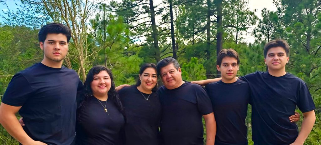 The Fierro-Rayas Family, all posing together in front of green trees, all dressed in black