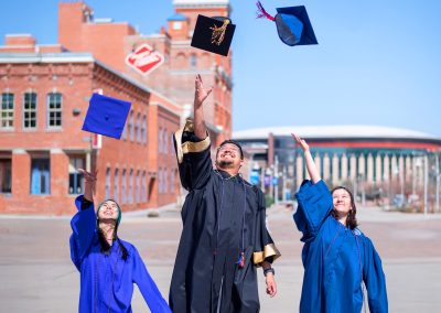 Three DSF Scholars throw their graduation caps into the sky in front of the Tivoli on Auraria Campus