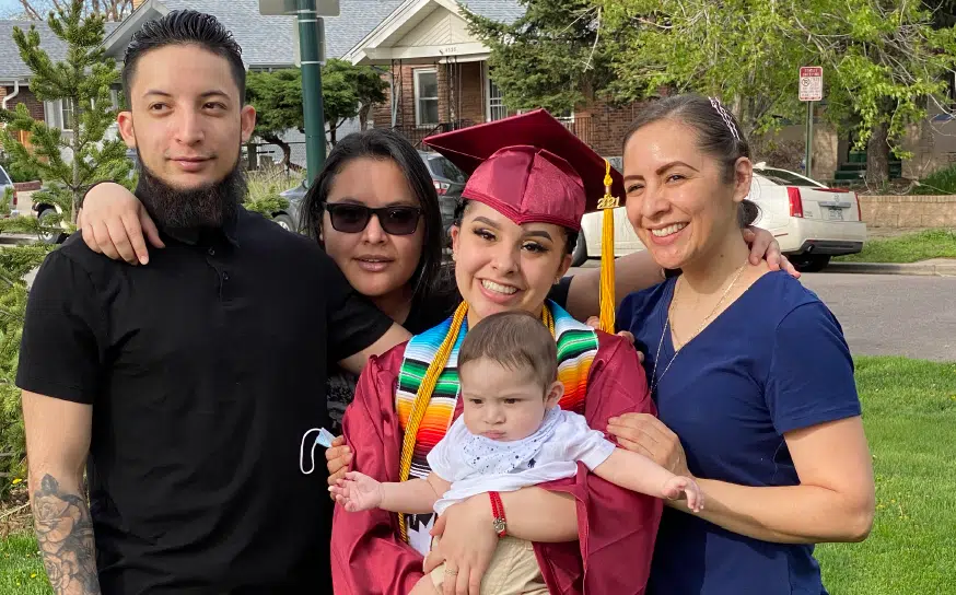 Deysi smiles in her cap and gown, holding her baby and posing with her family