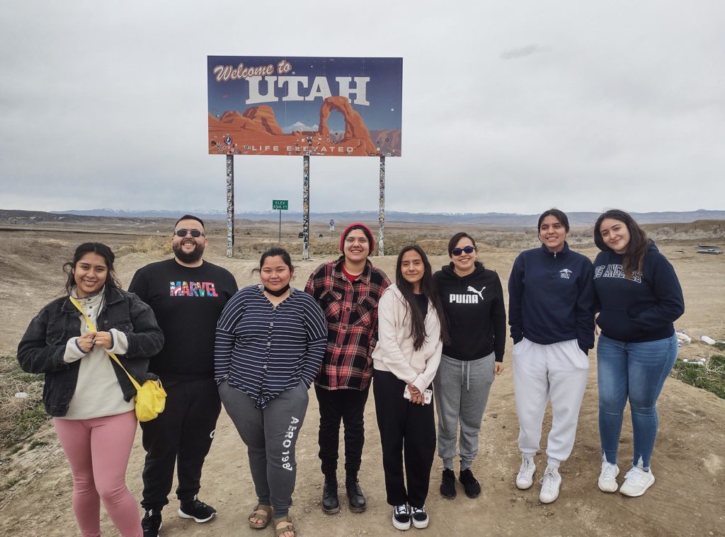 Pricilla and a group of students posing in front of "Welcome to Utah" sign outside
