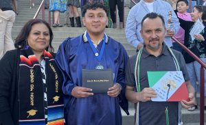 Erick Plata standing in the middle with his parents the day of his high school graduation holding his diploma