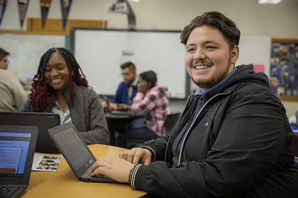 become a scholar Student smiles away from his computer at the DSF Future Center. Another student is sitting with him as they work on financial aid applications.