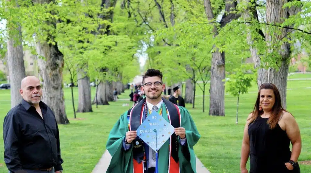 Brayan Montes standing in a graduation cap and gown with his family on graduation day, smiling proudly together.